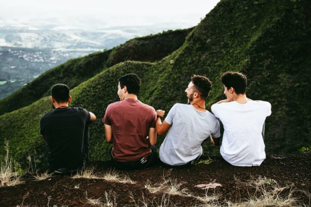 a group of friends sitting on a cliff high up in the mountains and laughing