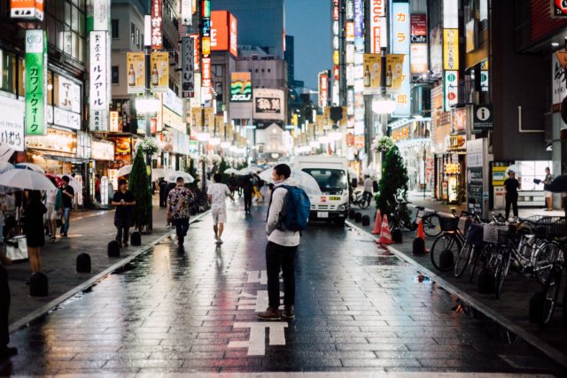 a man standing in the middle of the road of a busy metropolis in Japan during a rainy night.