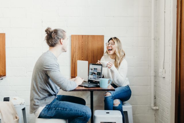 a man and a woman sitting on a dining table in a café and having an amusing conversation