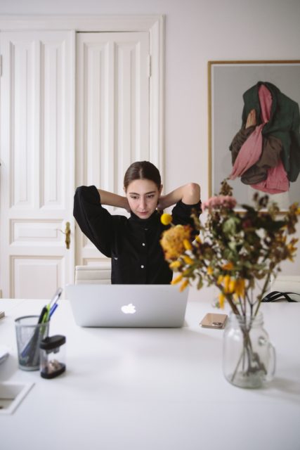 woman in black blouse sitting in front of silver laptop preparing for a virtual interview
